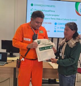 Emerson, profissional da Refap, recebendo do Cacique Cirilo kit sobre o projeto com aldeias Guarani no RS